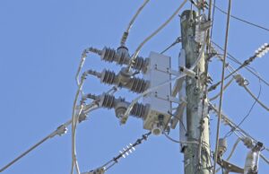 Electric Utility Infrastructure::A close-up view of electric utility equipment mounted on a wooden power pole against a clear blue sky.
