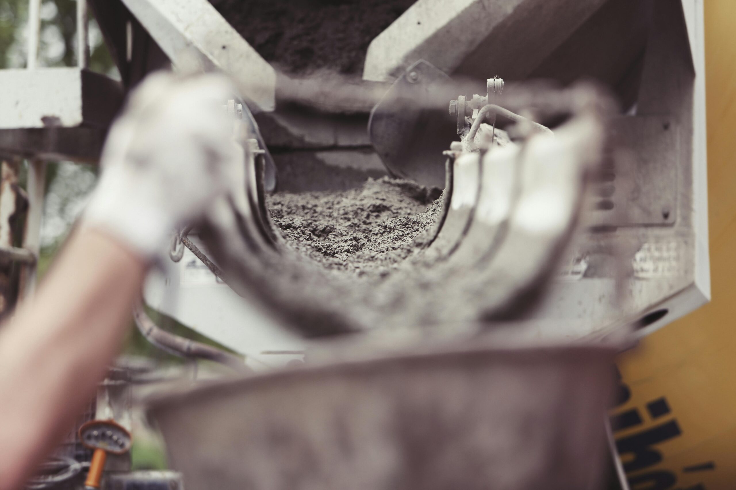A close-up view of a worker pouring wet concrete from a mixer into a container at a construction site.